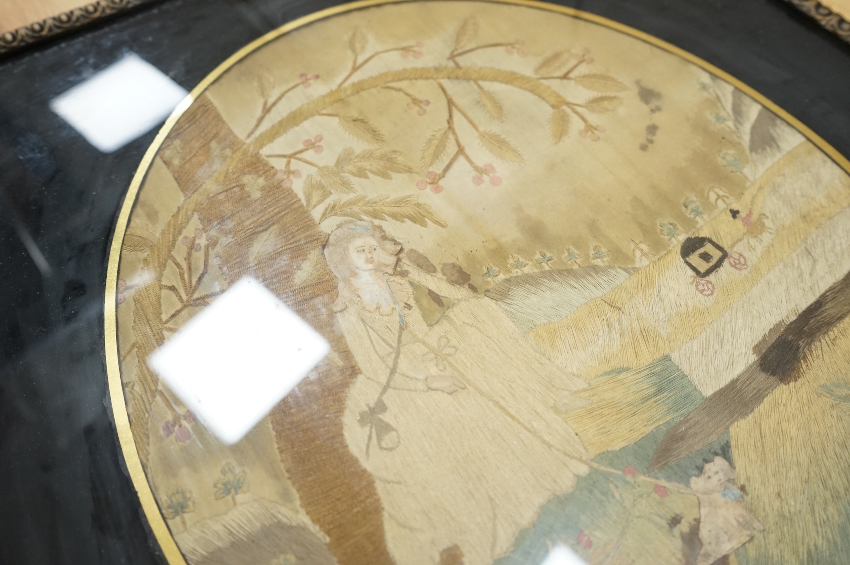 An early 19th century framed oval silk embroidery of a woman with a dog, overall 48cm high